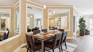 Un comedor con una mesa grande dispuesta para seis personas, rodeada de sillas, en una habitación con espejos en las paredes y una planta en maceta.