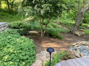 A garden with a wooden deck, a stone pathway, and various plants.