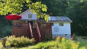 Una casita con terraza de madera, un paraguas rojo y paneles solares en el techo.