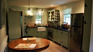 Una cocina con armarios verdes, una mesa de comedor de madera y un refrigerador de acero inoxidable.
