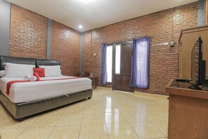 Una habitación de hotel con pared de ladrillo, cama con ropa de cama blanca y almohada roja, un escritorio de madera y una puerta con cortinas moradas.