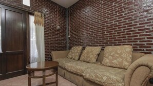 A room with a brick wall, a wooden door, a beige sofa with floral cushions, and a small wooden table. - RedDoorz Plus @ Ampera Raya (Jakarta)