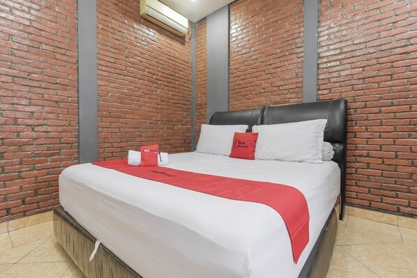 Habitación de hotel con pared de ladrillo, cama con ropa de cama blanca y detalles rojos, y una manta roja.