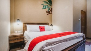 Un lit bien fait, avec une couverture rouge, une tête de lit en bois et une lampe fixée au mur.