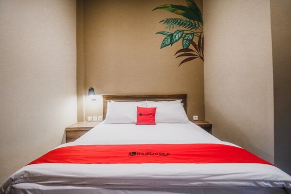 Une chambre d’hôtel avec un lit, une table de chevet, une lampe fixée au mur et une plante.