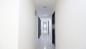 A long, narrow hallway with white walls and a shiny floor, leading to a door at the end. - RedDoorz @ Baloi Batam (Batam)