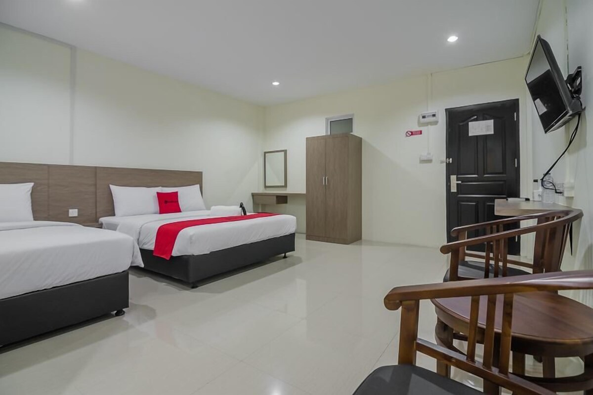 A hotel room with two beds, a wooden wardrobe, a desk with a chair, and a TV mounted on the wall.