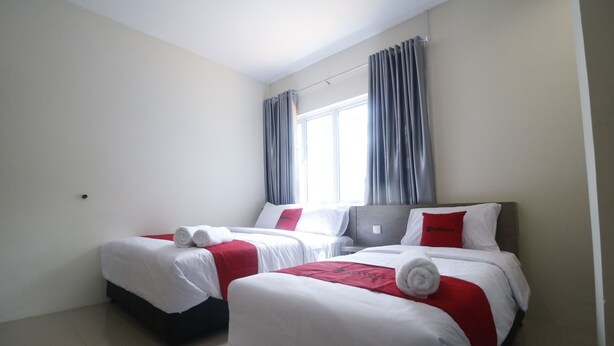 A hotel room with two beds, each with white bedding and red accents, a large window with curtains, and a plain wall. - RedDoorz @ Baloi Batam (Batam)