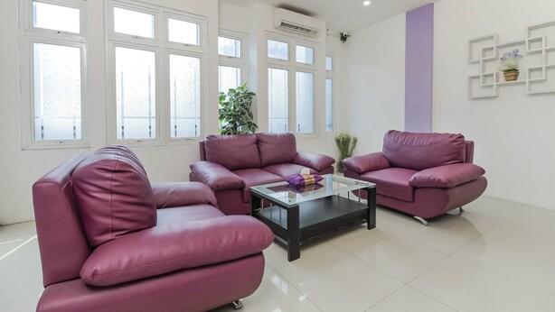 Ein modernes Wohnzimmer mit zwei violetten Sofas, einem Glastisch und großen Fenstern.