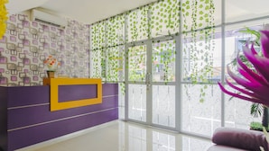 Ein Empfangsbereich mit einem violett-gelben Empfangstresen, einem großen Fenster mit grünen Pflanzen und einem spiegelnden Boden.