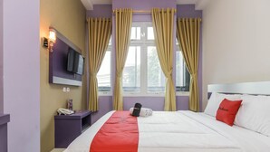 Ein Hotelzimmer mit Bett, Wandfernseher, Nachttisch mit Telefon und einem Vorhangfenster.