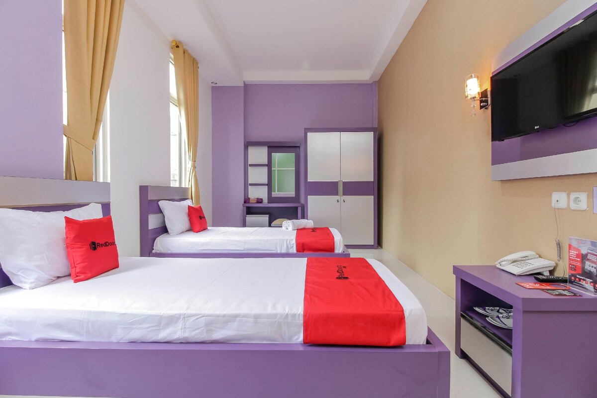 Ein Hotelzimmer mit zwei Betten, einem Fernseher, einem Schreibtisch mit Telefon und einem Spiegel.