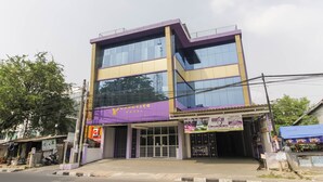 Ein mehrstöckiges Gebäude mit einer violett-gelben Fassade, ein großer Glasvordereingang und eine Beschilderung für 'Yuruyivo Hotel'.