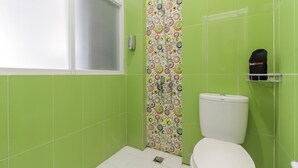 Ein Badezimmer mit grünen Fliesen, einer Toilette, einer Dusche mit farbigem Rundmuster und einem RedDoorz Handtuchhalter.