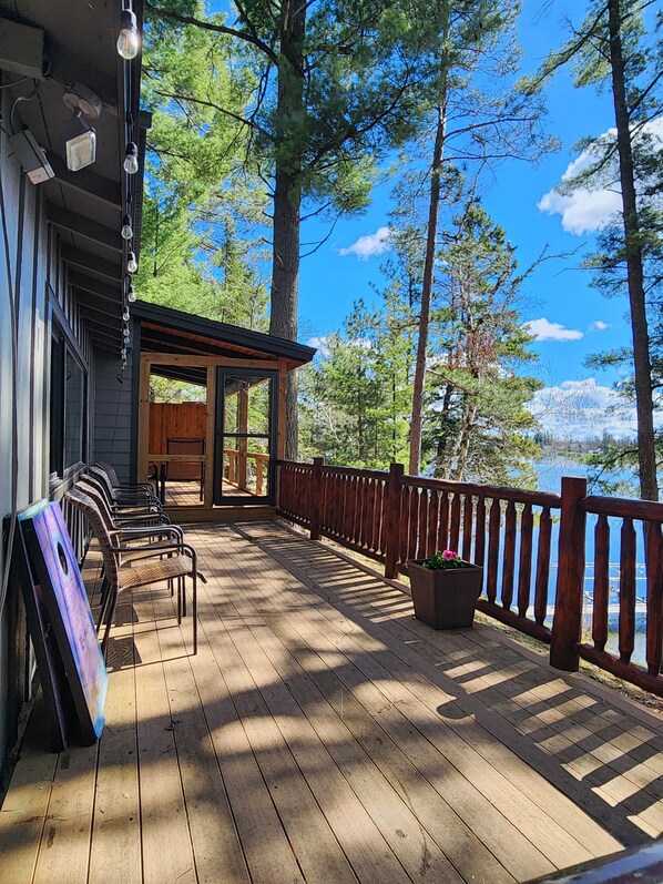 A wooden deck with outdoor seating, a small building, and a view of trees and a lake.