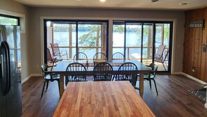 A dining area with a wooden table and chairs, large windows with a view of a lake, and a ceiling with recessed lighting. - Rustic Log Cabin/Modern Addition - Pontoon, Bunk House, Hot Tub - Woman Chain (Longville)