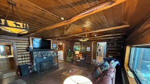 A cozy cabin interior with a stone fireplace, a large sofa, a television, and a wooden ceiling. - Rustic Log Cabin/Modern Addition - Pontoon, Bunk House, Hot Tub - Woman Chain (Longville)