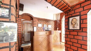 Een receptiegedeelte met een bakstenen muur, een houten receptiebalie en ingelijste foto's.