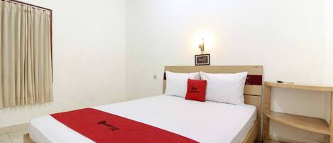 Habitación de hotel con cama, mesita de noche, manta roja y lámpara de pared.
