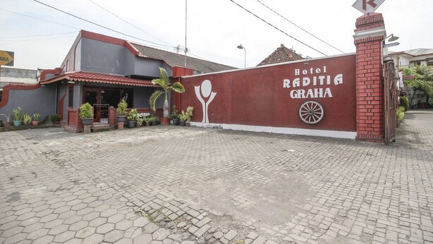 Een hotelentree met een rode bakstenen muur, een bord met Hotel Raditia Graha en een parkeerbord.