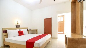 Een hotelkamer met een bed, een houten hoofdbord, een nachtkastje, een rood kussen, een rode plaid en een houten deur, plus een groot raam.