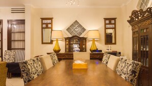 A formal dining room with a long wooden table, patterned chairs, and two wall-mounted lamps. - RedDoorz near Gasibu Bandung (Bandung)