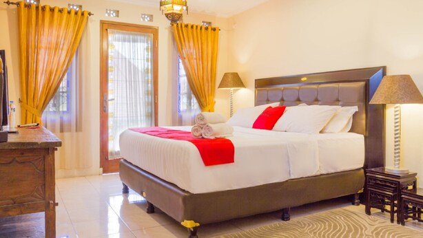 A hotel room with a large bed, a wooden dresser, and a patterned rug. - RedDoorz near Gasibu Bandung (Bandung)