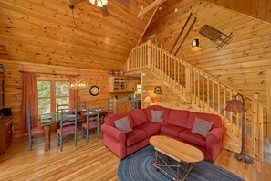 Interior acogedor de una cabaña con escalera de madera, un sofá rojo, zona de comedor y cocina.