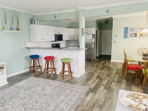 A kitchen with white cabinets, a central island with stools, and a dining area with a table and chairs.