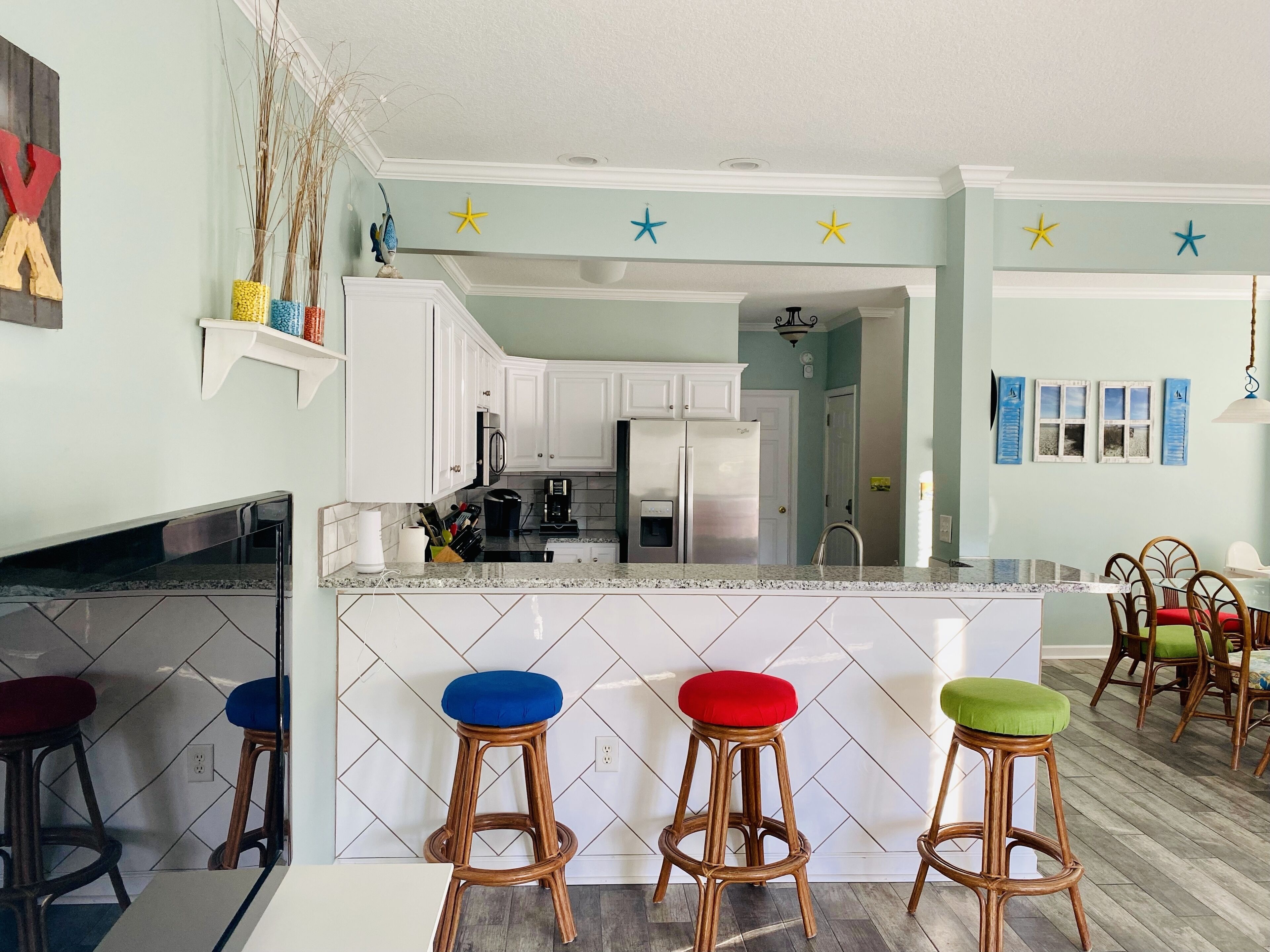 A kitchen with white cabinets, a central island with stools, and a dining area with chairs.