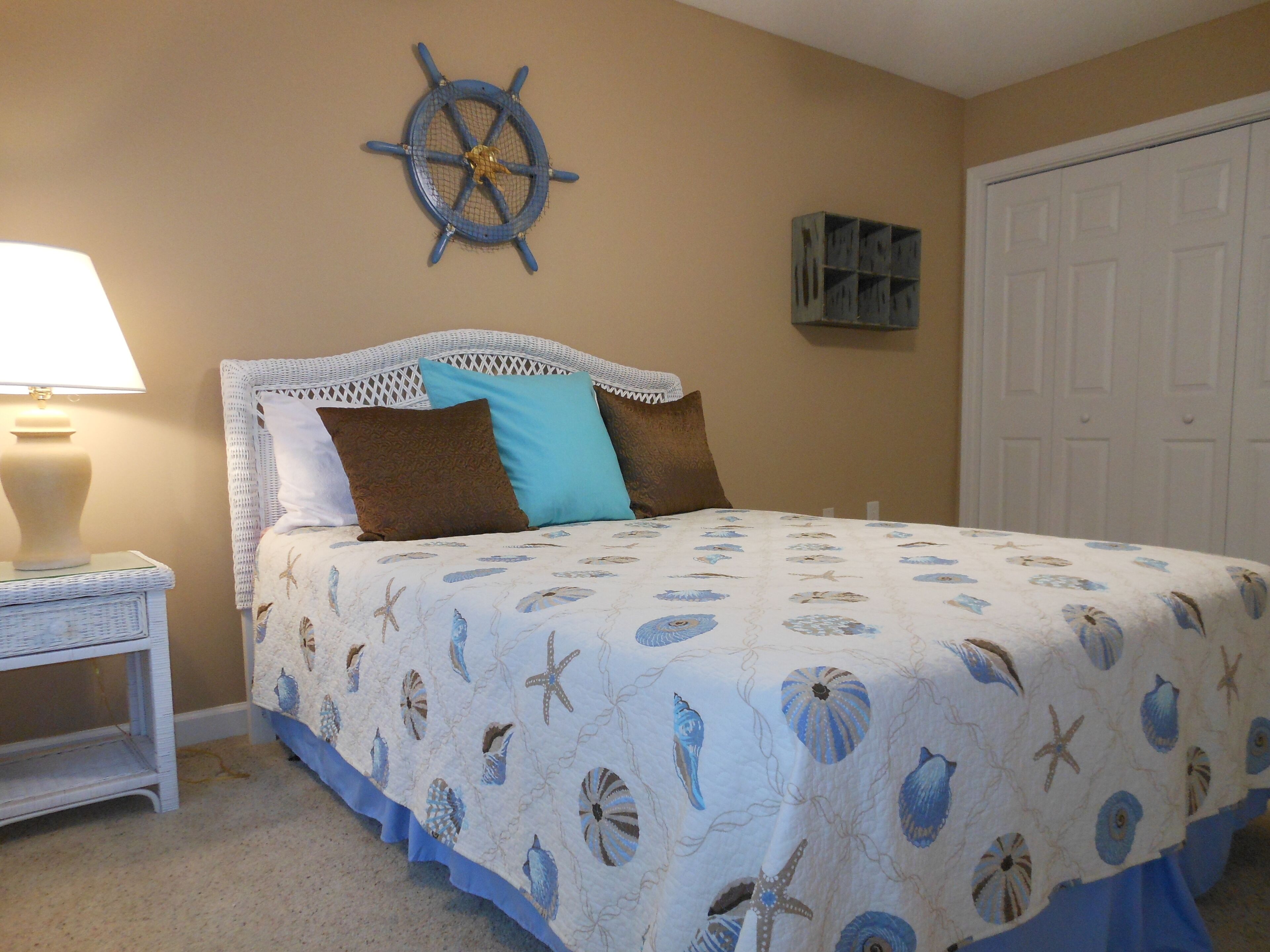 A bedroom with a bed, a nightstand, a wall-mounted ship's wheel, and a door.