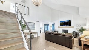 Uma sala de estar ampla com escada, um sofá marrom grande, uma mesa de jantar e uma TV fixada na parede.