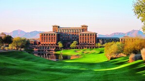 Um hotel grande com vários edifícios, um campo de golfe bem cuidado e montanhas ao fundo.