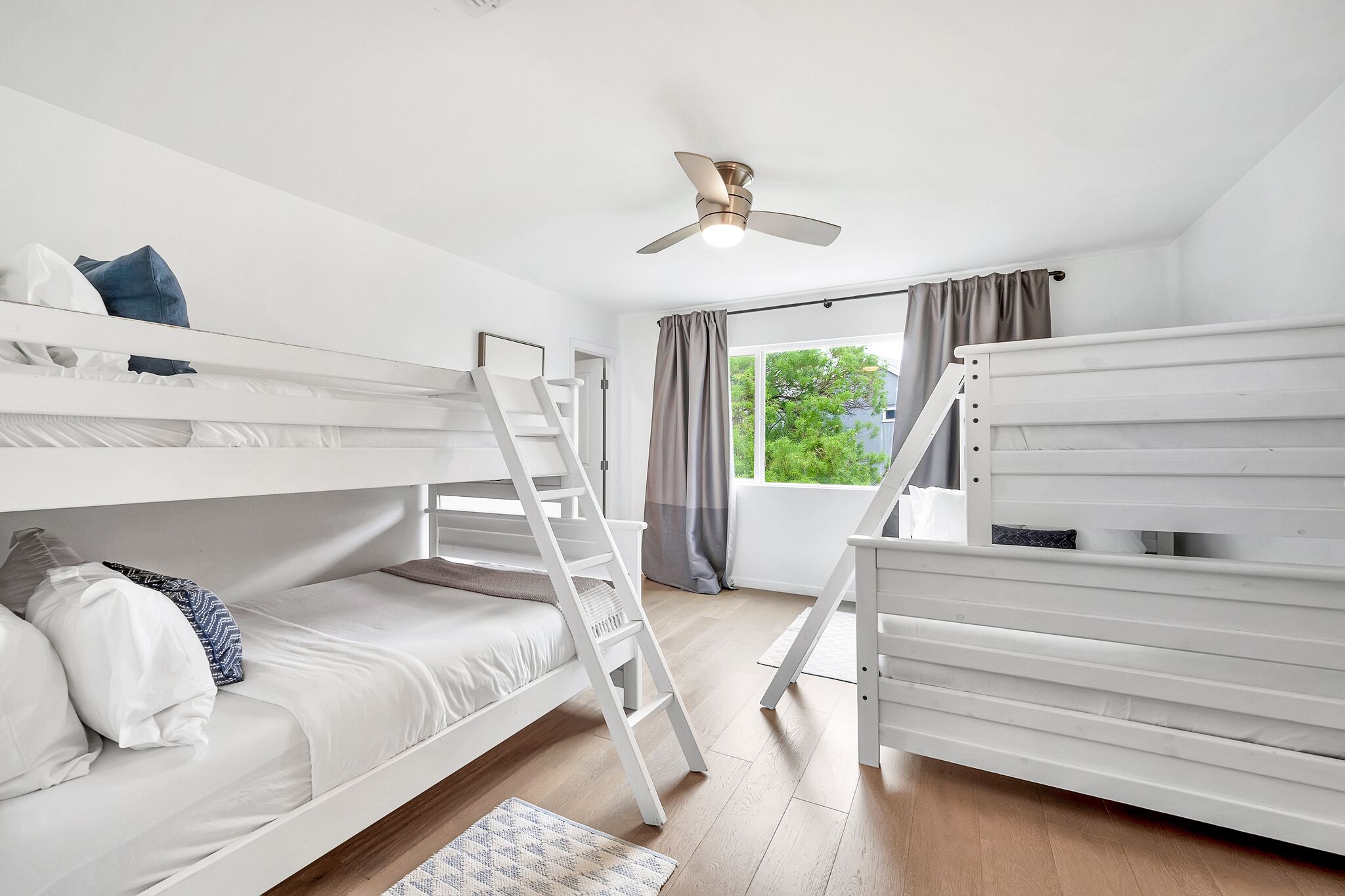 A room with bunk beds, a ceiling fan, and a window with curtains.