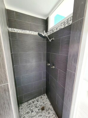 A shower with a handheld showerhead, dark tiled walls, and a pebble-patterned floor.