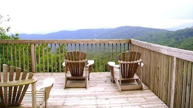 Una terraza de madera con sillas Adirondack y una mesa, con vistas a un paisaje montañoso.