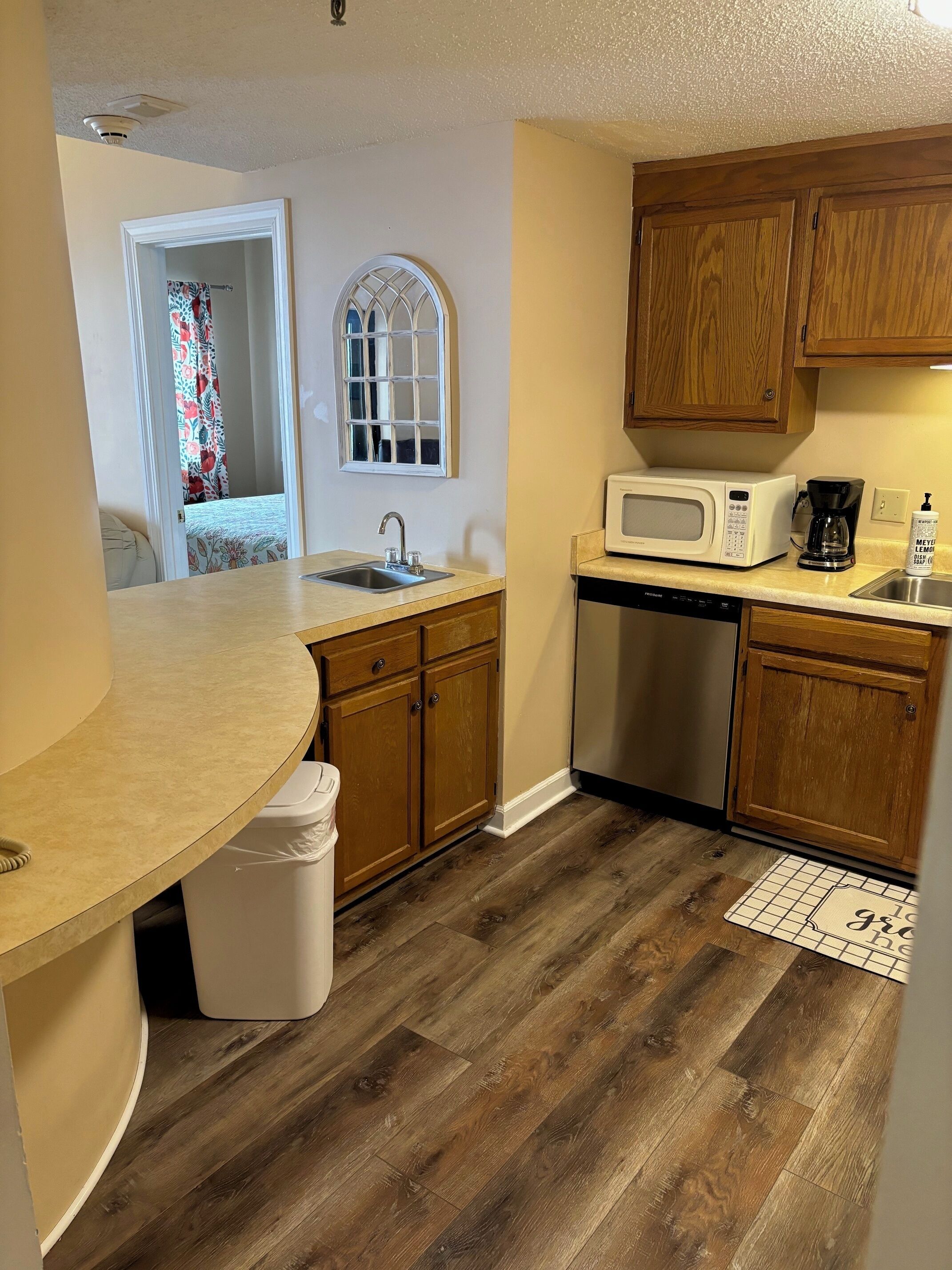 A compact kitchen with wooden cabinets, a microwave, a coffee maker, and a sink.