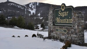 Señal de Sugar Mountain Skiing, con un muro de piedra y vistas a un paisaje nevado y una montaña al fondo.