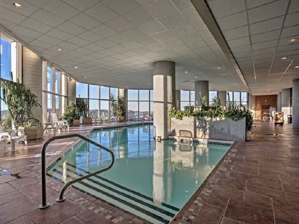 An indoor swimming pool with clear glass walls, large windows, and potted plants.