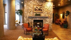 Un hall con chimenea de piedra, dos sillones, una mesa con un jarrón y un cuadro grande sobre la chimenea.