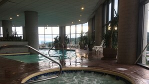 Una amplia piscina interior con un jacuzzi en el centro, rodeada de sillones de descanso y plantas en macetas.