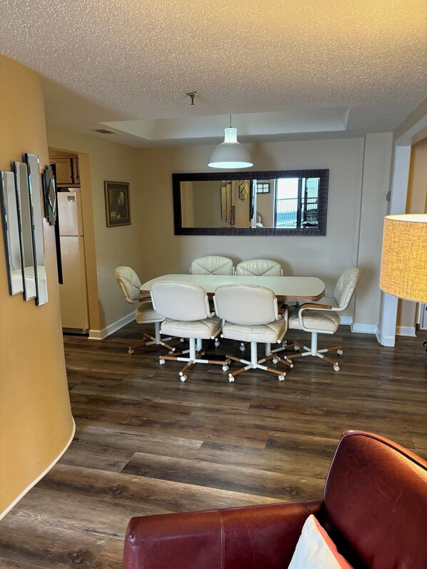 A modern living room with a dining area, featuring a large mirror, a chandelier, and a leather sofa.