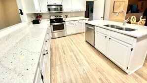 Une cuisine moderne avec des meubles blancs, des appareils en acier inoxydable et un plan de travail en granit.