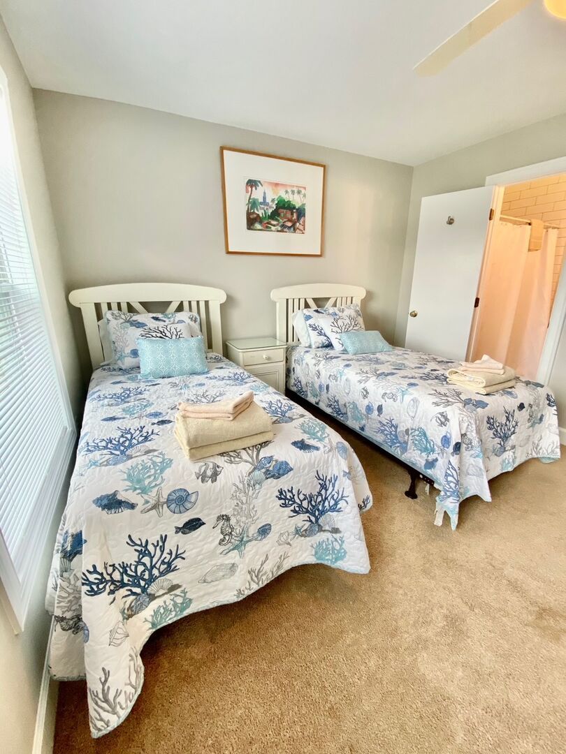 Une chambre à coucher avec deux lits, chacun agrémenté d’une couvre-lit aux motifs coralliens bleus et blancs, d’une tête de lit blanche et d’une petite table de chevet.