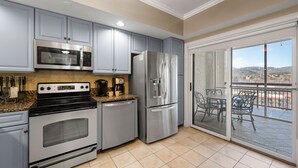 A modern kitchen with stainless steel appliances, grey cabinets, and a sliding glass door leading to a balcony with outdoor furniture.