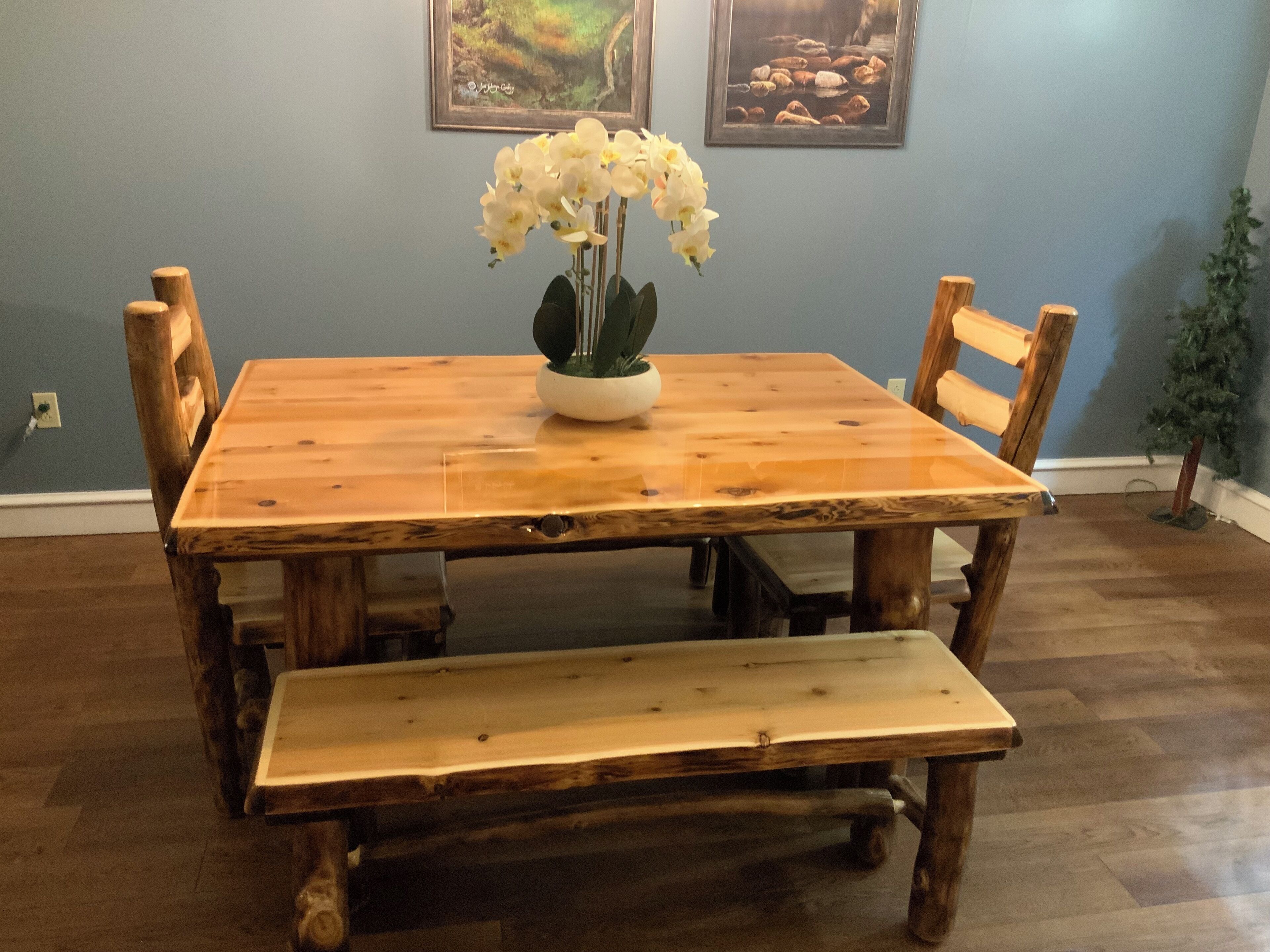 A wooden dining table with a bench, surrounded by chairs, in a room with a blue wall and a small potted plant.