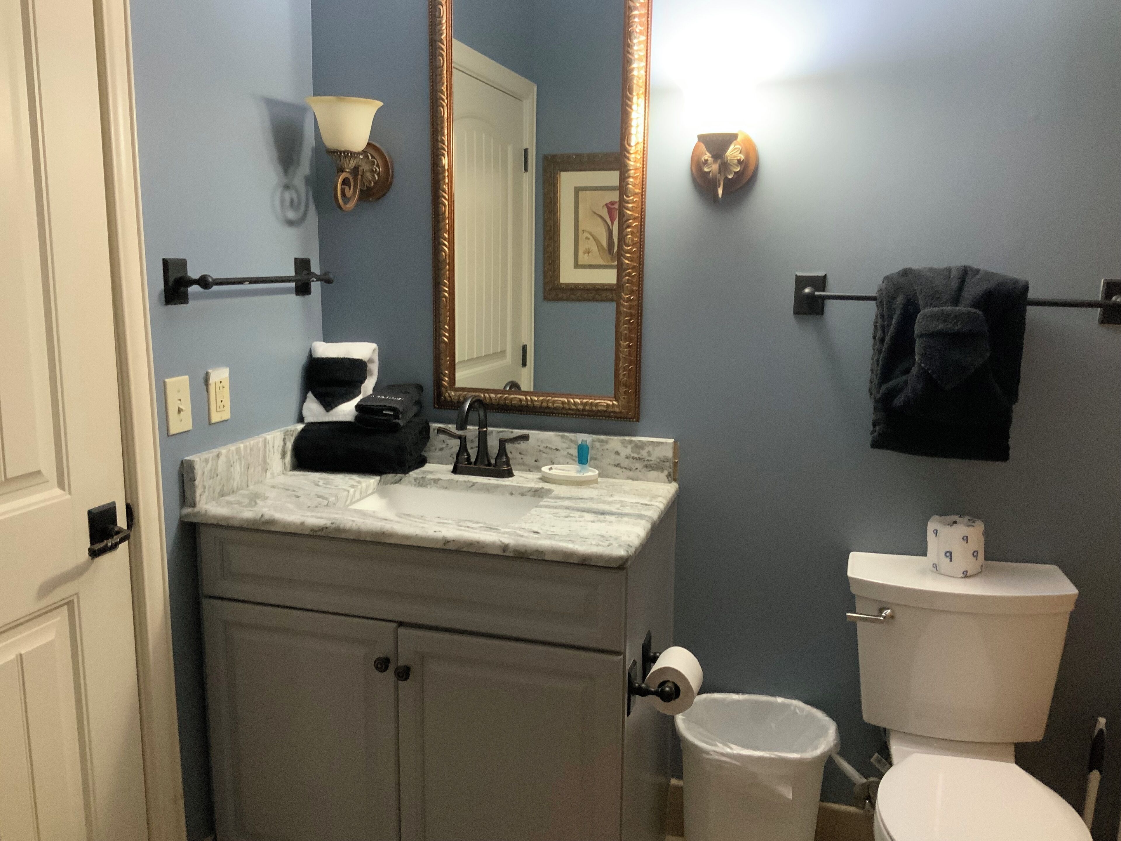 A bathroom with a sink, mirror, toilet, and a trash can.