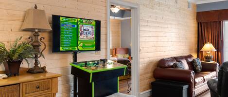 Una habitación acogedora con mesa de fútbol, televisor montado en la pared, sofá de cuero y suelo de madera.