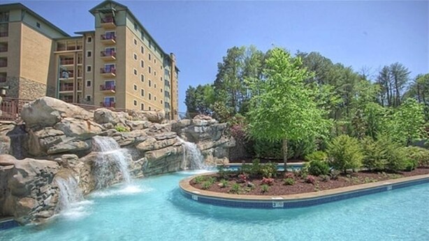 A hotel with a pool featuring a waterfall and a landscaped area with trees.