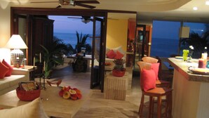 A spacious living area with a view of the ocean, a ceiling fan, and a dining area with a bar.